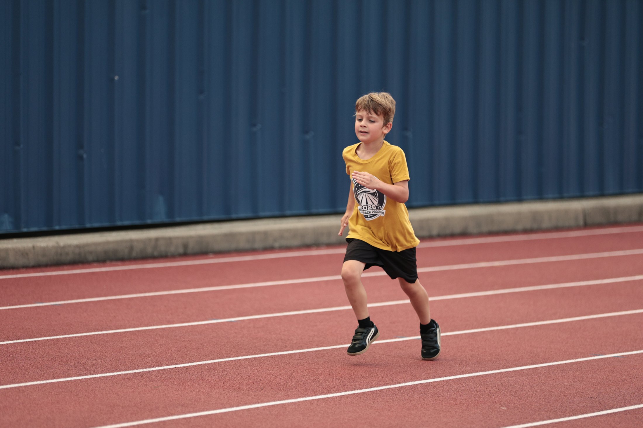 Young runner near a blue track wall.